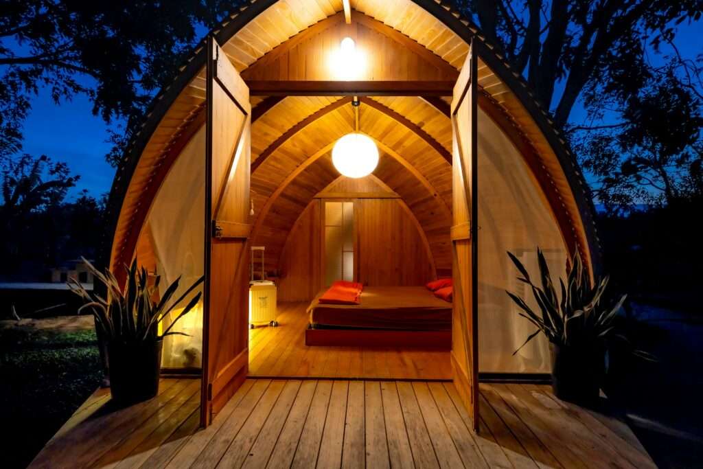 Warmly lit wooden cabin with open doors at night, showcasing cozy interior and unique architecture.